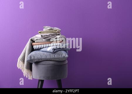 Stapel sauberer Bettlaken und Kissen auf dem Hocker vor violettem Hintergrund. Platz für Text Stockfoto