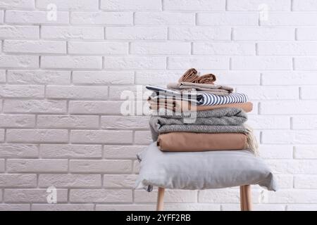 Stapel sauberer Bettlaken und Kissen auf dem Hocker nahe der weißen Backsteinwand. Platz für Text Stockfoto