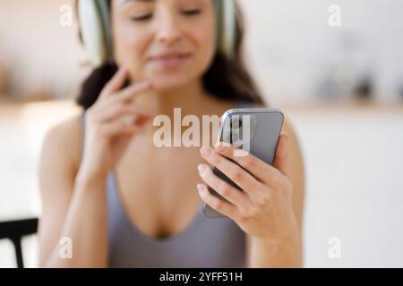 Die junge Frau entspannt sich zu Hause mit Kopfhörern, verloren in der Musik auf ihrem Smartphone. Sie genießt eine friedliche Pause und lächelt zufrieden in einer ruhigen Umgebung Stockfoto