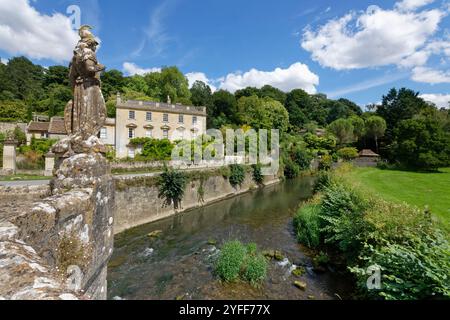 Statue von Britannia auf einer Brücke über den Frome mit Iford Manor und dem Peto-Garten im Hintergrund, in der Nähe von Bradford-on-Avon, Wiltshire, Großbritannien. Stockfoto