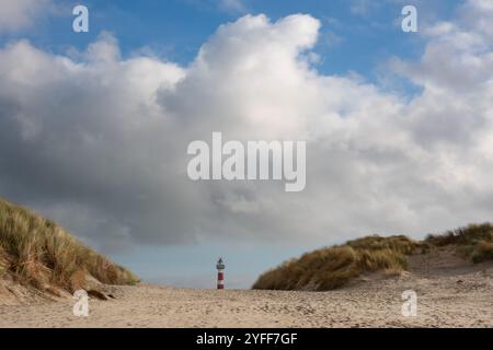 Blick zwischen zwei Dünen auf den rot-weißen Leuchtturm der niederländischen Insel Ameland Stockfoto