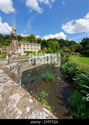 Statue von Britannia auf einer Brücke über den Frome mit Iford Manor und dem Peto-Garten im Hintergrund, in der Nähe von Bradford-on-Avon, Wiltshire, Großbritannien. Stockfoto