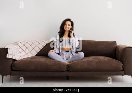 Die junge Frau sitzt zu Hause auf ihrer Couch, trägt Sportkleidung und lächelt nach dem Training Stockfoto