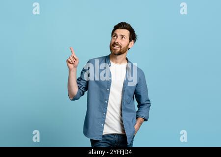 Happy man zeigt mit dem Finger auf den Kopierraum, während er auf einen blauen Hintergrund blickt Stockfoto
