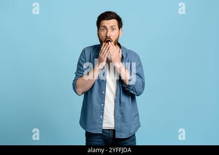 Der junge Mann bedeckt seinen Mund mit den Händen und sieht schockiert aus von etwas, das er gerade gesehen hat Stockfoto