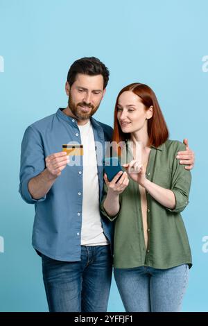 Ein Mann und eine Frau machen einen Online-Kauf mit einem Smartphone und einer Kreditkarte und stehen dicht beieinander auf blauem Hintergrund Stockfoto