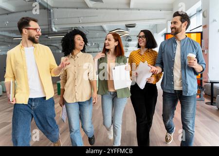 Eine Gruppe von Kollegen läuft gemeinsam durch das Büro, spricht und lacht Stockfoto