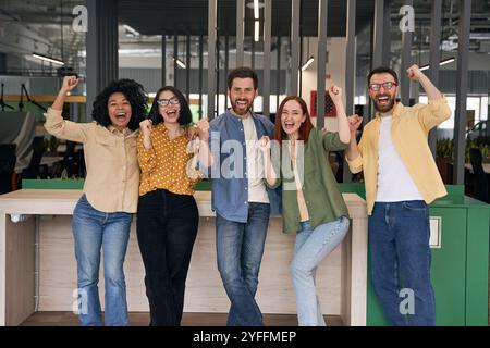 Eine vielfältige Gruppe von Fachleuten feiert den Erfolg, indem sie in einer modernen Büroumgebung mit Begeisterung ihre Fäuste in die Luft heben Stockfoto