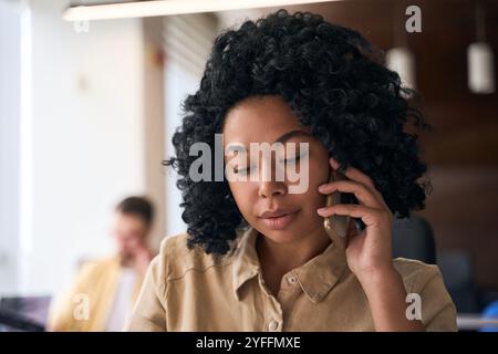 Eine konzentrierte junge Managerin spricht an ihrem Telefon, während sie in einem geschäftigen Open-Space-Büro arbeitet Stockfoto