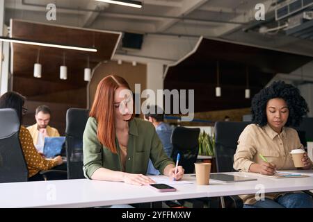 Junge Büromitarbeiter konzentrieren sich auf ihre Arbeit, während sie an Schreibtischen in einem modernen Co-Working-Raum sitzen Stockfoto