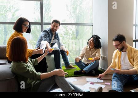 Verschiedene Designer-Teams führen ein produktives Brainstorming durch, bei dem sie Haftnotizen und digitale Tablets verwenden, um innovative Ideen zu entwickeln Stockfoto