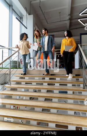 Eine Gruppe multiethnischer Kollegen, die nach der Arbeit die Treppe im Büro hinuntergingen, sprachen und lächelten Stockfoto
