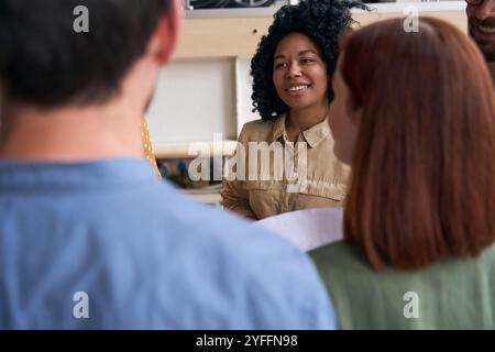 Die junge Geschäftsfrau lächelt, während sie ihrem Team bei einem zwanglosen Büromeeting Ideen vorstellt Stockfoto