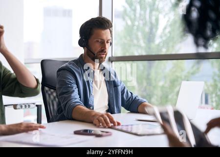 Ein fokussierter männlicher Callcenter-Agent arbeitet an seinem Computer in einem Großraumbüro Stockfoto