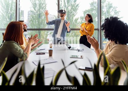 Ein Team von Kollegen applaudiert einem Mann, der ein vr-Headset verwendet, während einer Geschäftspräsentation im Büro Stockfoto