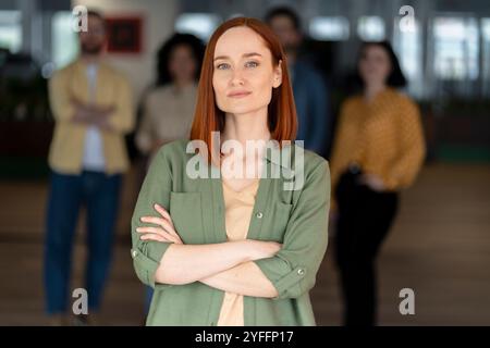 Geschäftsfrau steht mit überkreuzten Armen und einem selbstbewussten Ausdruck, der ihr Team zum Erfolg führt Stockfoto