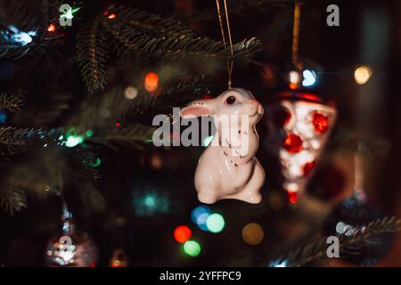 Festliches Weihnachtsspielzeug in Form von weißem Kaninchen, das an den Zweigen des Weihnachtsbaums hängt. Neujahrsdetails und -Einrichtung Stockfoto