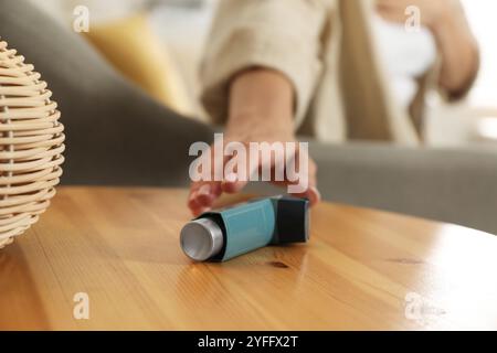 Frau, die nach Asthma-Inhalator greift, an Holztisch drinnen, Nahaufnahme Stockfoto