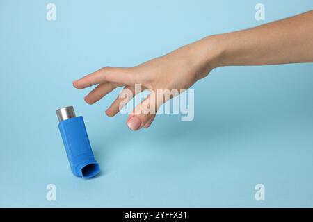 Frau, die nach einem Asthma-Inhalator auf hellblauem Hintergrund greift, Nahaufnahme Stockfoto