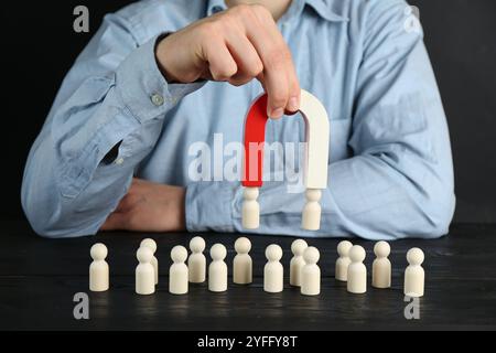 Mann mit Magnet, der menschliche Figuren an einem schwarzen Holztisch anzieht, Nahaufnahme Stockfoto