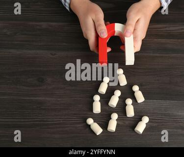 Mann mit Magnet, der menschliche Figuren an einem Holztisch anzieht. Leerzeichen für Text Stockfoto