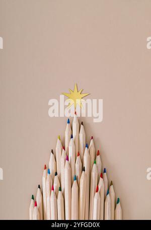 Weihnachtsbaum aus farbigen Bleistiften auf pastellfarbenen cremefarbenen Hintergrund. Minimales Weihnachts- und Neujahrskonzept. Kreatives festliches Layout. Flache Lagen. Stockfoto