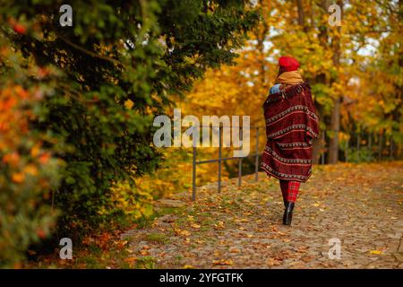 Hallo Herbst. Von hinten gesehen Frau mit rotem Hut und Schal, die im Stadtpark spaziert. Stockfoto