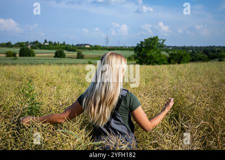 Eine Frau mit fließenden langen Haaren, die einen sonnigen Tag in einem atemberaubenden und leuchtenden gelben Blumenfeld genießt Stockfoto