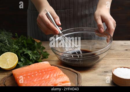 Frau, die Sojamarinade für Lachsfilet am Holztisch macht, Nahaufnahme Stockfoto