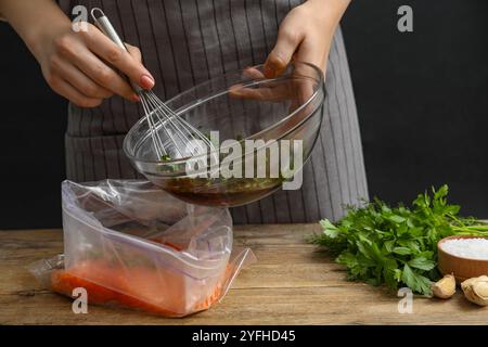 Frau mit Sojamarinade und Lachsfilet in Plastiktüte am Holztisch, Nahaufnahme Stockfoto