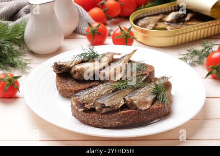 Köstliche Sandwiches mit Sprotten und Dill, serviert auf weißem Holztisch, Nahaufnahme Stockfoto