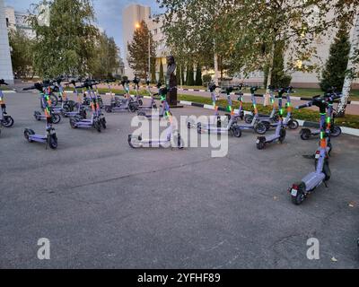 Große Anzahl von Elektromotorrollern, die auf einem Platz zurückgelassen wurden; Lichter blinken; blaue Motorroller Stockfoto