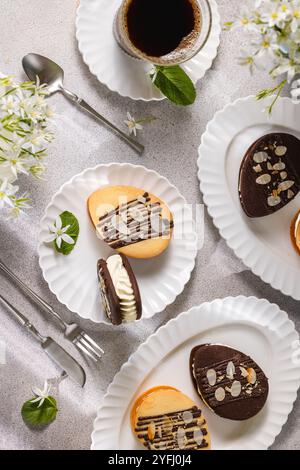 Köstliche, mit Sahne gefüllte, mit Schokolade und Mandeln dekorierte ostereier, serviert auf weißen Tellern mit Kaffee und Blumen Stockfoto