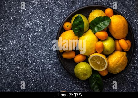 Lebendige Zitrusfrüchte, einschließlich Zitronen, Limetten, Kumquats und Orangen, erstellen Sie ein farbenfrohes Arrangement auf einem dunklen Teller, das ihre Frische und V zum Ausdruck bringt Stockfoto