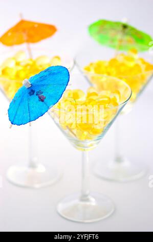Drei Martini-Gläser gefüllt mit Kabeljau-Leberöl-Kapseln, Quellen von Vitamin A, Vitamin d und Omega-3, dekoriert mit Mini-Sonnenschirmen über weißem Hintergrund Stockfoto