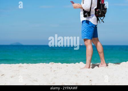 Junger Mann reist mit einer professionellen DSLR-Kamera im Freien an einem tropischen Strand mit blauem Himmel und weißer Wolke. Machen Sie ein Foto im Urlaub mit der Liebe zur Natur Stockfoto