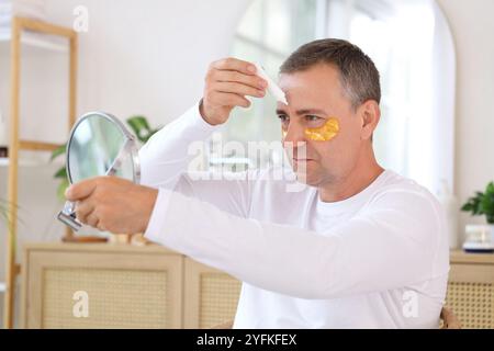 Reifer Mann in Augenflecken mit Spiegel, Creme auftragen und Gesichts-Building-Übungen zu Hause machen Stockfoto