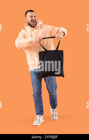 Glücklicher junger Mann mit Textiltasche auf orangem Hintergrund Stockfoto