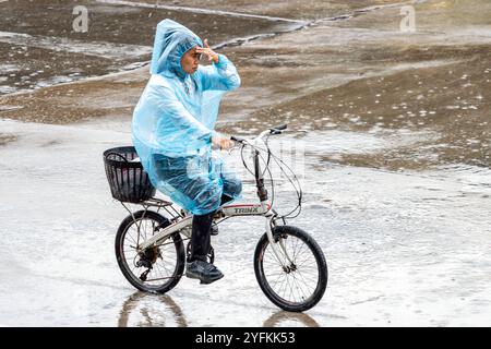 SAMUT PRAKAN, THAILAND, 04. Oktober 2024, Eine Frau im Regenmantel fährt im Regen mit dem Fahrrad Stockfoto