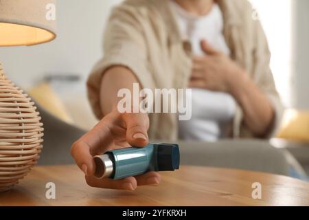 Frau hält Asthma Inhalator an Holztisch drinnen, Nahaufnahme Stockfoto