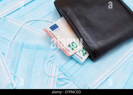 Schwarze Herren Brieftasche mit Euro Geld innen auf den blauen Einweg-medizinischen Gesichtsmasken. Handel mit medizinischen Masken. Unternehmen während einer Pandemie oder Epidemie Stockfoto