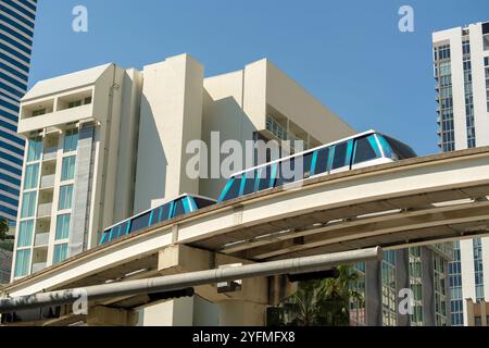 Öffentliche Verkehrsmittel im Zentrum von Miami in Florida, USA. Metrorail-Stadtzugwagen auf hoher Eisenbahn über Straßenverkehr zwischen Wolkenkratzergebäuden in Stockfoto