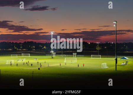 Öffentliches Sportstadion mit jungen Leuten, die bei Sonnenuntergang ein Fußballspiel spielen. Aktives Lebenskonzept. Stockfoto