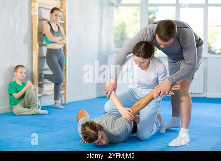 Beim Selbstverteidigungstraining vermittelt der Trainer Frauen die Technik, den Arm zu greifen und den Gegner auf den Boden zu senken Stockfoto