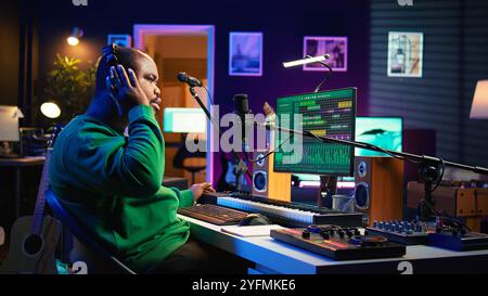 Ein professioneller Künstler schreibt neue Verse für einen Song im Heimstudio und produziert neue Musik mit einer Mischkonsole und pc-Software. Composer arbeitet mit Audiogeräten und -Tools und nimmt Lieder auf. Kamera B.. Stockfoto