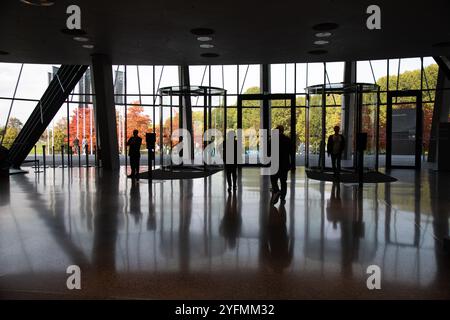 Silhouetten von Personen, die aus dem Bürogebäude in Richtung Drehtüren mit Reflexionen auf dem Boden gehen Stockfoto