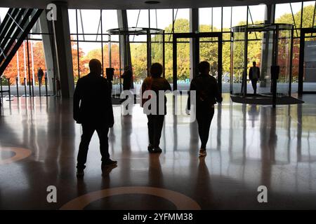 Silhouetten von Personen, die aus dem Bürogebäude in Richtung Drehtüren mit Reflexionen auf dem Boden gehen Stockfoto