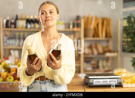 Die Käuferin untersucht Bierflaschen, wählt den richtigen Hersteller, nimmt verschiedene Flaschen aus dem Regal. Stockfoto