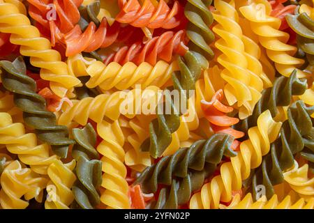 Ungekochte Fusilli Pasta in leuchtenden Farben: Eine faszinierende kulinarische Leinwand aus bunten Spiralen, die einen lebendigen und strukturierten Hintergrund für Gourmet-Kochen schafft. Farbige Trockene Pasta. Rohe Makkaroni Stockfoto