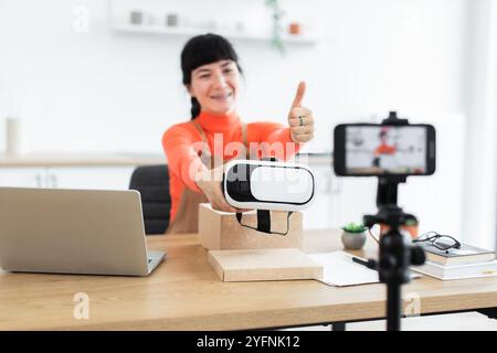 Die weiße Bloggerin entpackt aufgeregt das neue Virtual-Reality-Headset, während sie online streamt. Sie zeigt eine VR-Brille vor der Kamera, zeigt die Daumen hoch, su Stockfoto